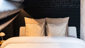 A bed with a headboard, pillows, and a lamp on a bedside table in a room with a stone wall.