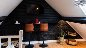 A cozy room with a black stone wall, two leather bar stools, a wooden table, a hanging light fixture, and a window.