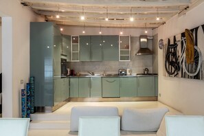 Una cocina moderna con armarios verdes, una campana extractora de acero inoxidable y un salpicadero de azulejos. En primer plano, hay dos zonas de estar con cojines blancos.