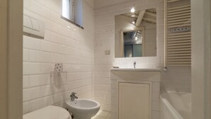 A bathroom with white tiled walls, a white toilet, a bidet, a sink, and a mirror. - The Borgias were here! Charming and modern, by Campo de’ Fiori (Roma)