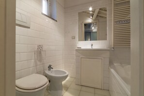 A bathroom with white tiled walls, a white toilet, a bidet, a sink, and a mirror.