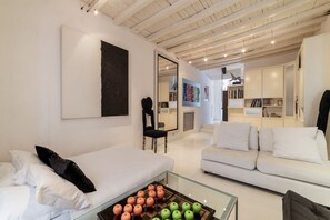 A modern living room with a glass coffee table, white sofas, and a large abstract painting.