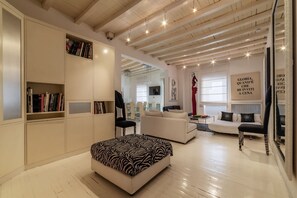 A modern living room with white furniture, a zebra-patterned ottoman, and a bookshelf.