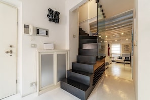 Una escalera moderna con barandilla de vidrio que conduce a una sala de estar con un sofá y un sillón.
