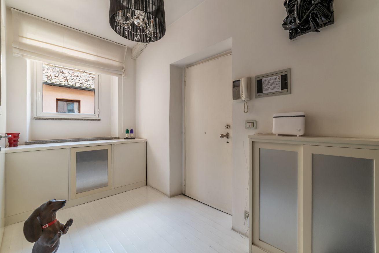 A narrow hallway with a window, a door, and a small cabinet with a phone and a thermostat.