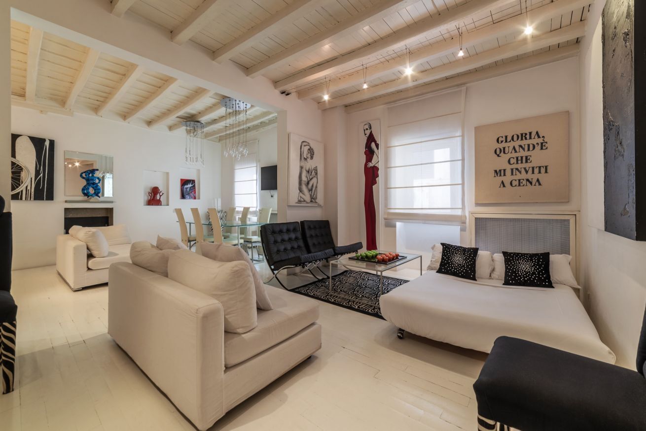 A modern living room with a sofa, armchairs, a dining area, and artwork on the walls.