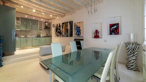 A modern interior with a glass dining table, white chairs, and a kitchen in the background. - The Borgias were here! Charming and modern, by Campo de’ Fiori (Roma)