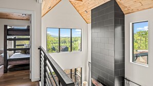 A modern interior with a wooden ceiling, a black tiled fireplace, and a view of a forest through large windows. - Serenity Now - Brand New Property/View/Indoor Pool/Hot Tub/Movie Room/Game Room (Sevierville)