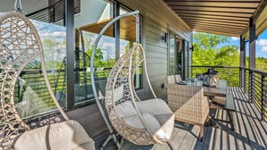A wooden deck with wicker chairs and a table, large windows, and a view of greenery. - Serenity Now - Brand New Property/View/Indoor Pool/Hot Tub/Movie Room/Game Room (Sevierville)