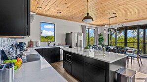 A modern kitchen with a large island, black cabinets, stainless steel appliances, and a wooden ceiling. - Serenity Now - Brand New Property/View/Indoor Pool/Hot Tub/Movie Room/Game Room (Sevierville)