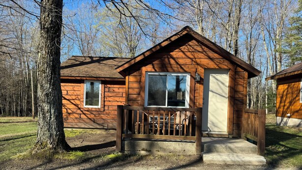A wooden cabin with a porch, a door, and a window. - Cozy 2 bedroom cottage with full kitchen minutes from Pictured Rocks Cruises! (Munising)