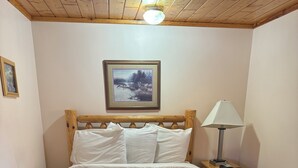A neatly made bed with a floral bedspread, a wooden headboard, a framed picture on the wall, and a bedside lamp. - Cozy 2 bedroom cottage with full kitchen minutes from Pictured Rocks Cruises! (Munising)