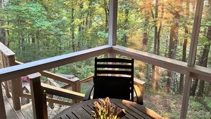 Um deck de madeira com uma mesa e cadeira, com vista para uma área arborizada onde a luz do sol se filtra pelas árvores.