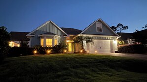 Une maison à deux étages avec un garage, entourée d’une pelouse bien entretenue et de quelques arbres.