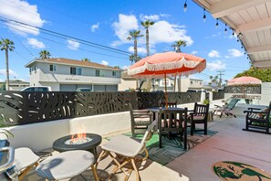An outdoor patio with wicker chairs, a fire pit, and two umbrellas. - Day in Paradise - O'side Palms (Oceanside)