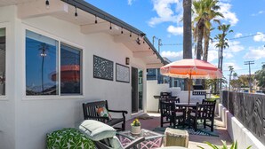 A patio with outdoor furniture, a table, and chairs. There is a large umbrella providing shade. - California Dreamin' - O'side Palms (Oceanside)