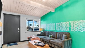 A modern living room with a green accent wall, a dark door, a wooden coffee table, and a patterned sofa. - California Dreamin' - O'side Palms (Oceanside)
