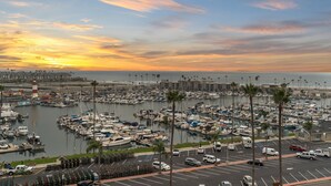 A marina with numerous boats docked, a parking area with cars, and a sunset in the background. - California Dreamin' - O'side Palms (Oceanside)