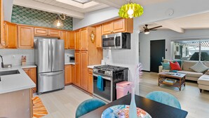 A modern kitchen with stainless steel appliances, wooden cabinets, and a dining area with a table and chairs. - Beach Meets Fabulous - O'side Palms (Oceanside)