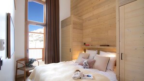 Ein gemütliches Schlafzimmer mit einem großen Bett, Holzwänden, einem Fenster mit Vorhängen und einem Sessel.