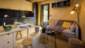 A modern kitchen with wooden cabinets, a dining table set for two, and a cozy living area with a sofa and a lamp. - Chalet Sideflip - cosy stay for 4 with wonderful views - OVO Network (La Clusaz)