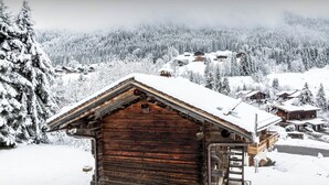 A wooden cabin with a snow-covered roof, surrounded by a snowy forest and other cabins. - Chalet Sideflip - cosy stay for 4 with wonderful views - OVO Network (La Clusaz)