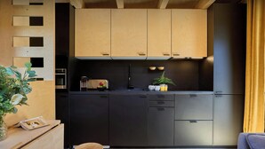 A modern kitchen with wooden cabinets, a black countertop, and a small stool. - Chalet Sideflip - cosy stay for 4 with wonderful views - OVO Network (La Clusaz)