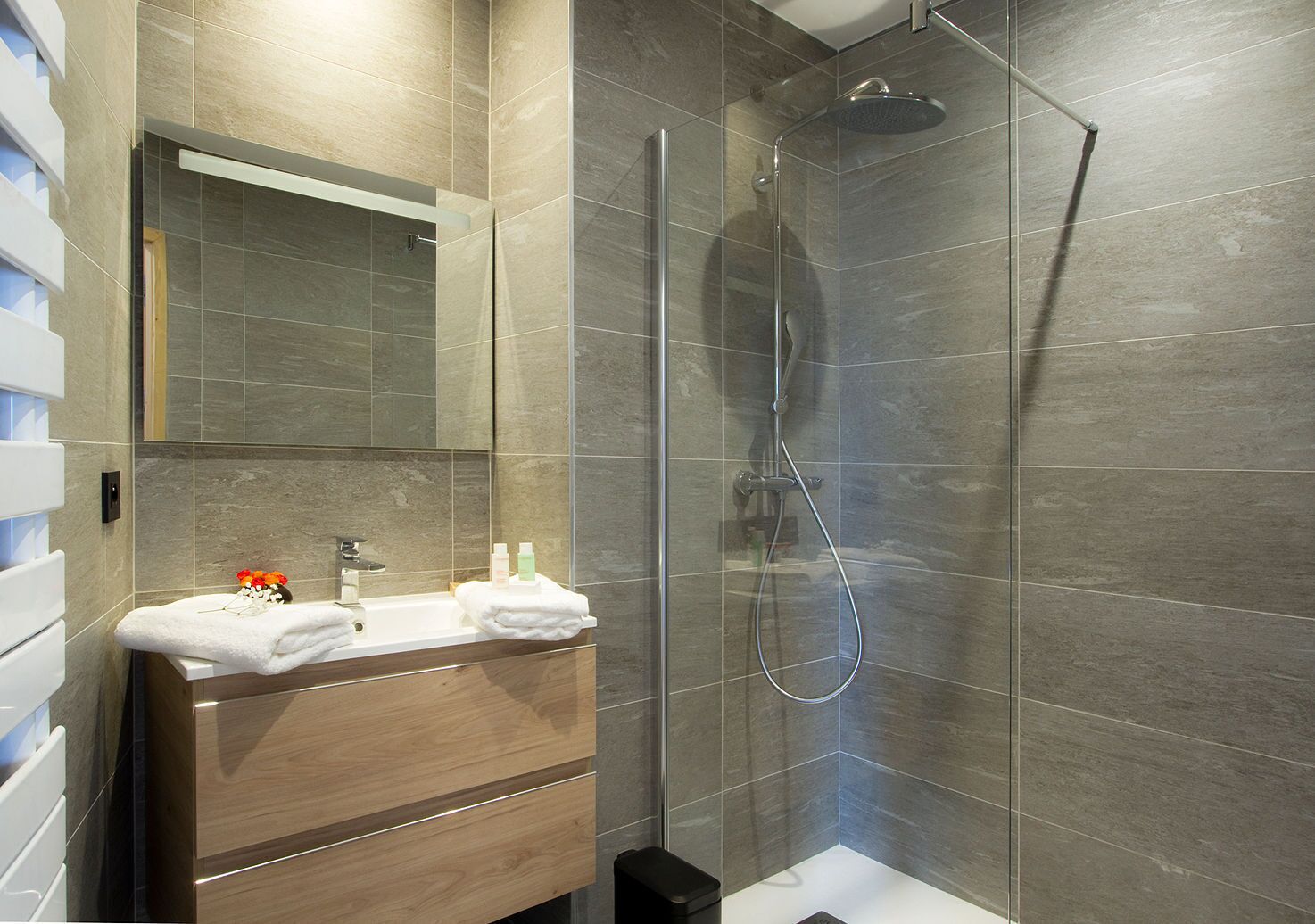A modern bathroom with a glass-enclosed shower, a wooden vanity with a mirror, and a white sink.