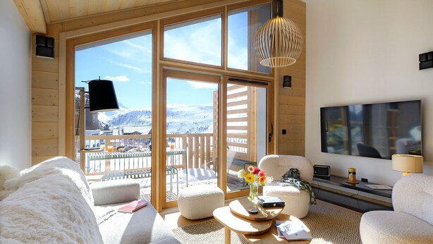 A cozy living room with a large window, a flat-screen TV, and a wooden ceiling.