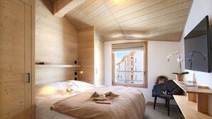 A cozy bedroom with a wooden ceiling, a large bed with a beige blanket, a desk with a chair, and a window with a view of buildings.