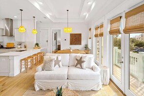 Un salon moderne avec un canapé blanc, une table à manger en bois et des luminaires suspendus.