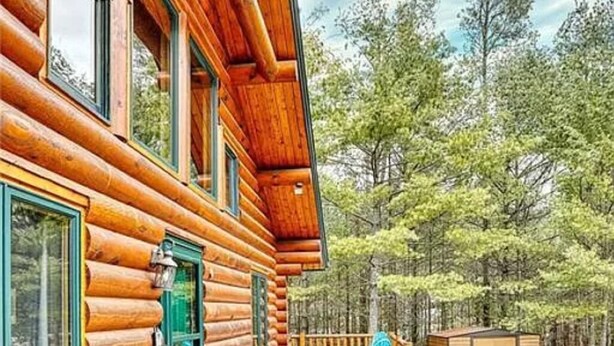 A log cabin with a wooden deck, a blue chair, and a small shed. - Spacious 3 Story Cabin. Access to UTV/ATV Trails & Near Lake Arbutus (Merrillan)