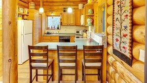 A log cabin interior with a kitchen area featuring wooden cabinets, a dining table with chairs, and a hanging light fixture. - Spacious 3 Story Cabin. Access to UTV/ATV Trails & Near Lake Arbutus (Merrillan)