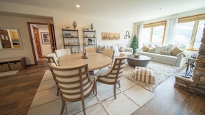 Ein geräumiges Wohnzimmer mit einem runden Esstisch, beigen Sofas und einem Kamin.