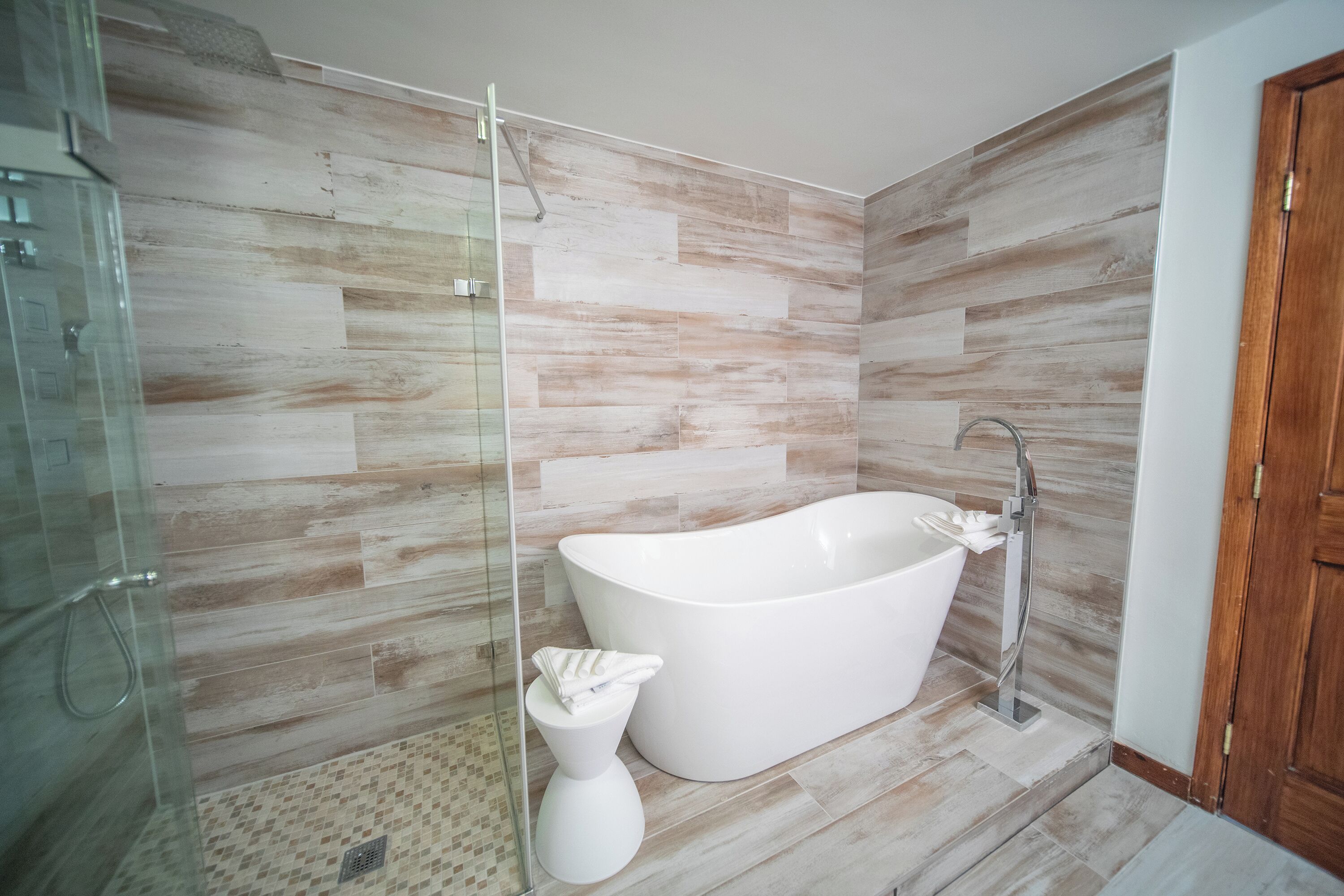 A modern bathroom with a freestanding bathtub, a glass shower enclosure, and a wooden floor.