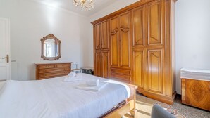 A bedroom with a large bed, wooden wardrobe, and a chandelier.