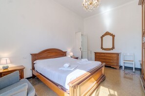 A bedroom with a wooden bed, a nightstand with a lamp, a dresser, a mirror, and a chair.