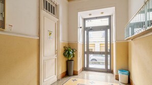 A hallway with a door, a potted plant, a trash bin, and a patterned floor.