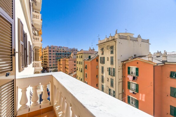 A balcony with a view of multi-story buildings, a clear sky, and a distant high-rise.