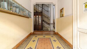 A hallway with a patterned floor, a glass railing on the left, and a staircase in the background.
