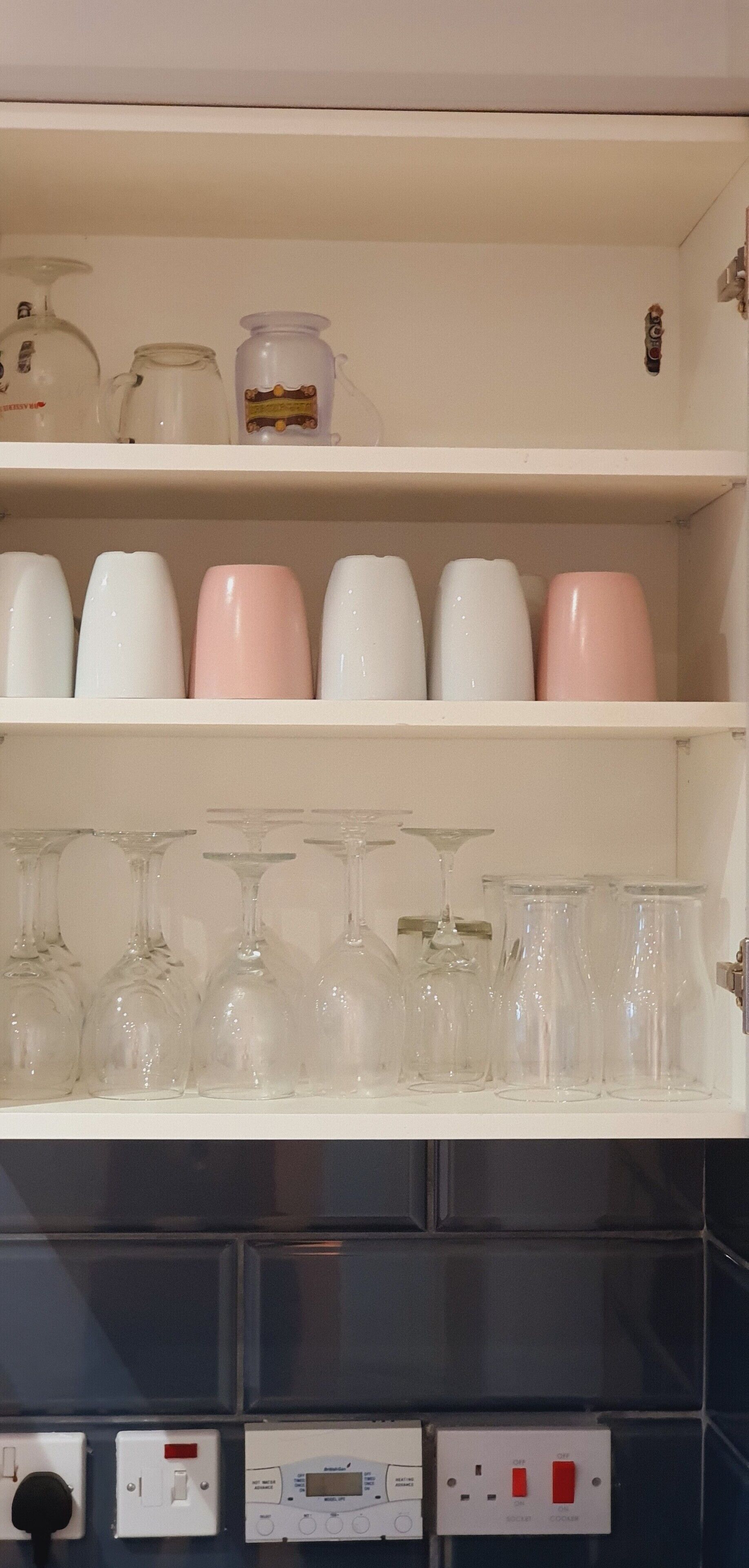A kitchen shelf with various glassware, including wine glasses and tumblers, and a few decorative jars.