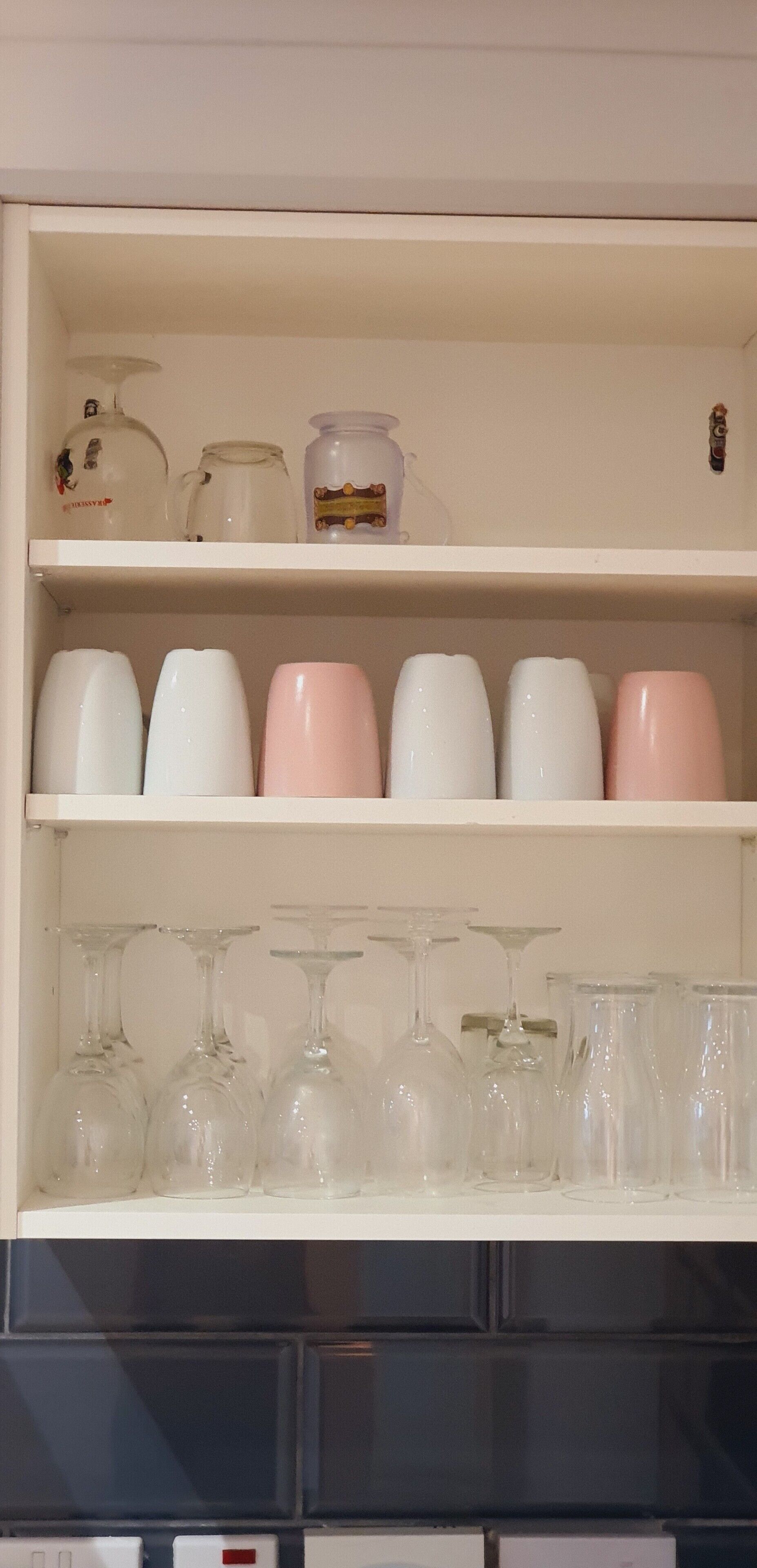 Un estante en la cocina con diferentes tipos de cristalería, incluyendo copas de vino y vasos.