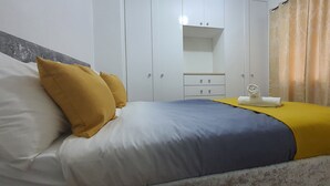 Ein Bett mit blauer und weißer Bettdecke, zwei gelbe Kissen und ein weißes Handtuch an einem hölzernen Kopfteil.