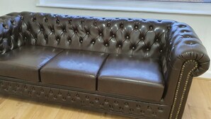 Ein braunes Ledersofa mit durchgesteppter Rückenlehne und Armlehnen, platziert in einem Raum mit Holzboden.