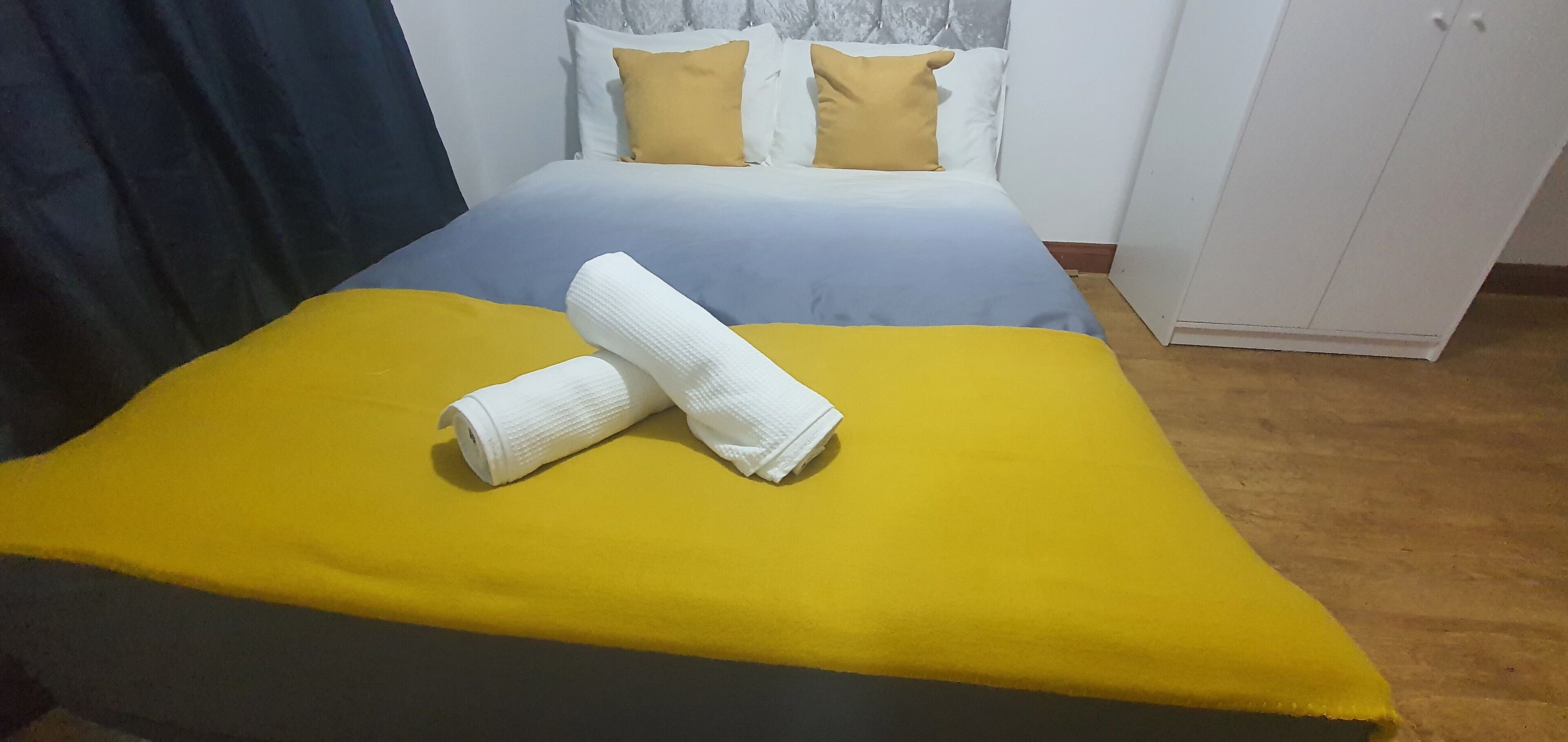 A bed with a yellow and blue bedspread, two white towels, and two yellow pillows.
