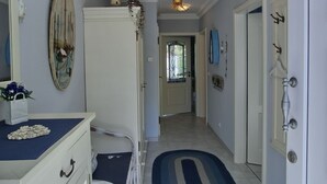 A hallway with a white dresser, a blue rug, a chandelier, and a door leading to another room.