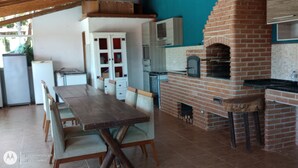 A kitchen with a brick oven, wooden table, and chairs. - Paraíso da Natureza (Ibiúna)