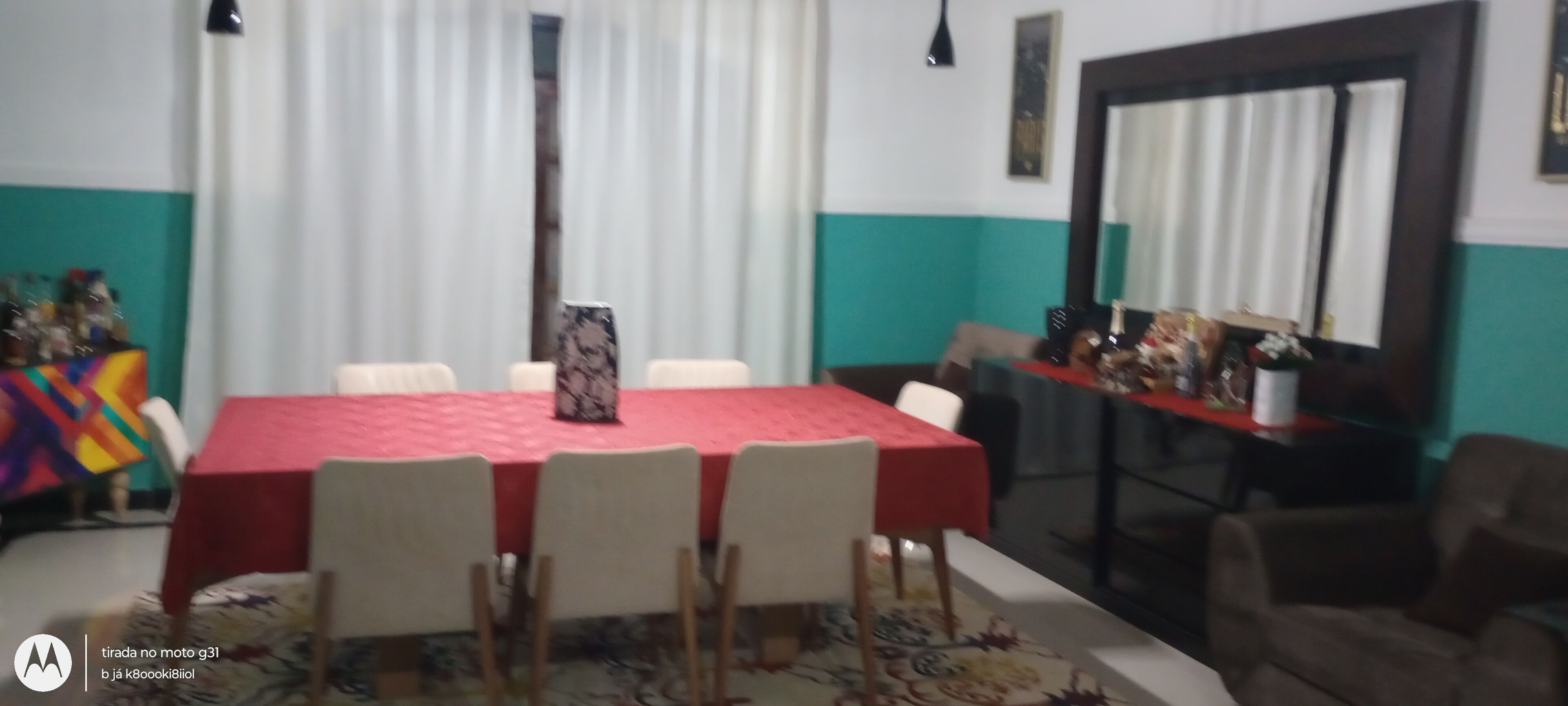 Un salón de conferencias con una mesa roja y sillas blancas. Hay un espejo grande en la pared y una ventana con cortinas.