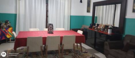 Un salón de conferencias con una mesa roja y sillas blancas. Hay un espejo grande en la pared y una ventana con cortinas.