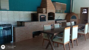 A kitchen with a brick oven, a gas stove, and a dining table with chairs. - Paraíso da Natureza (Ibiúna)
